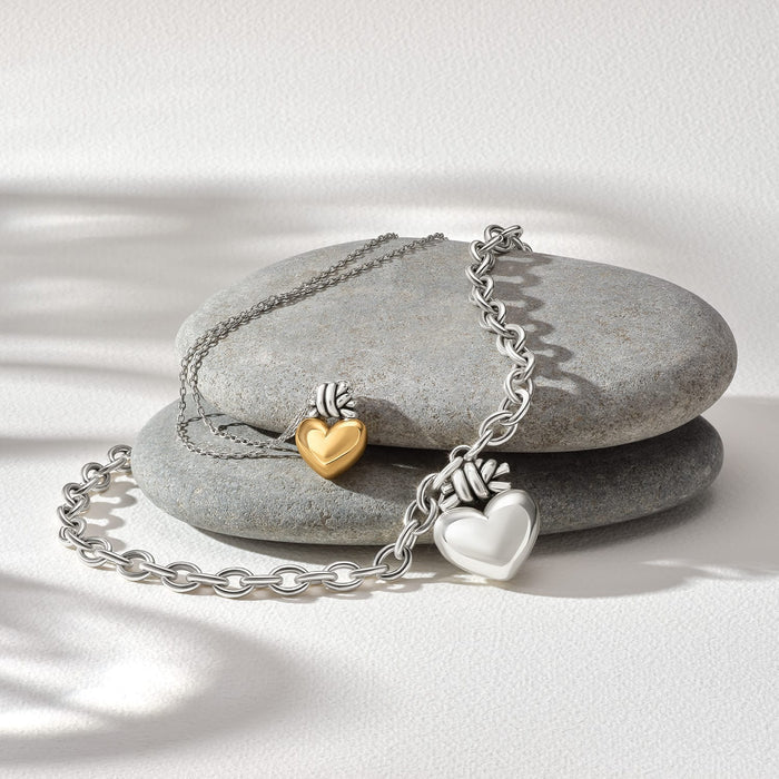 Brighton two-tone heart charms styled with smooth gray stones and silver chains on a neutral background