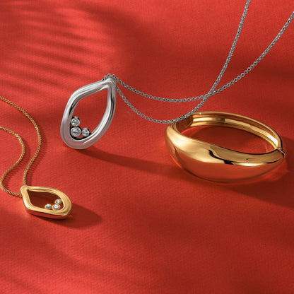 Brighton jewelry styled with silver-plated and gold-tone pendants and a gold bangle with crystals on red background