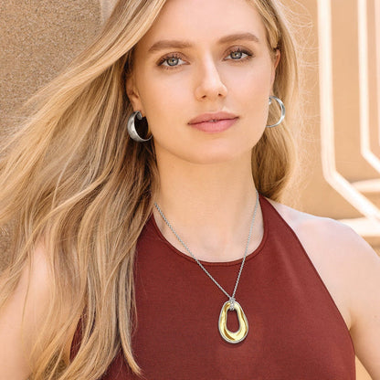 Model wearing a Brighton two-tone pendant necklace with silver and gold open teardrop, paired with silver hoop earrings