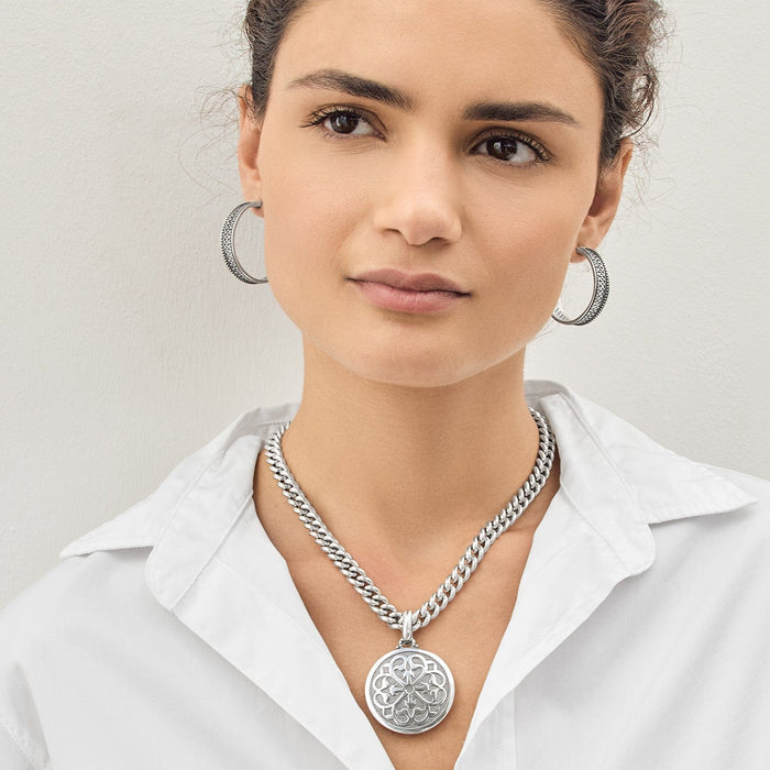 Model wearing a Brighton silver-plated curb chain necklace with ornate openwork medallion pendant and matching hoop earrings