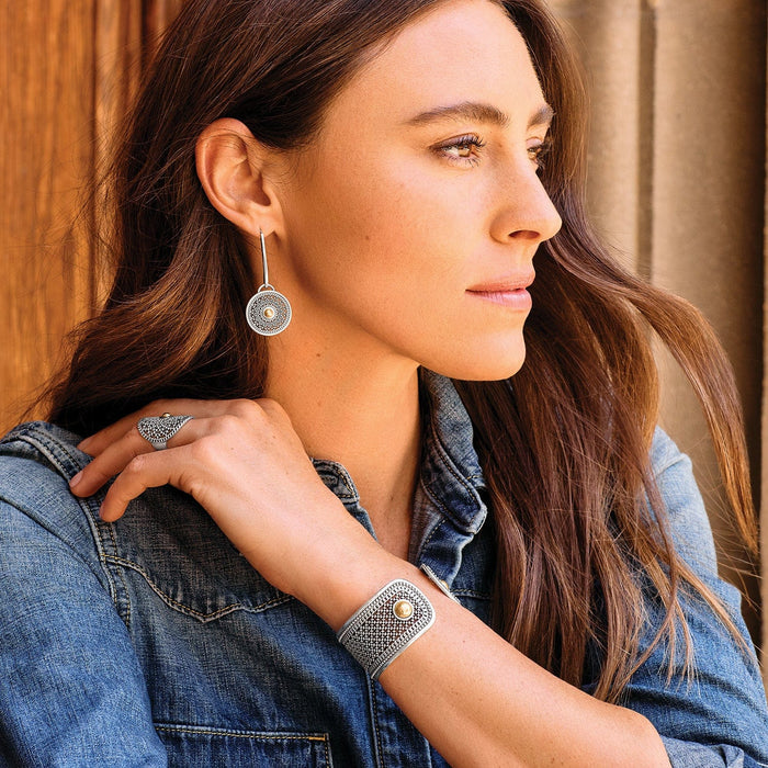 Model wearing Brighton two-tone medallion drop earrings with coordinating Brighton accessories including a ring and cuff bracelet