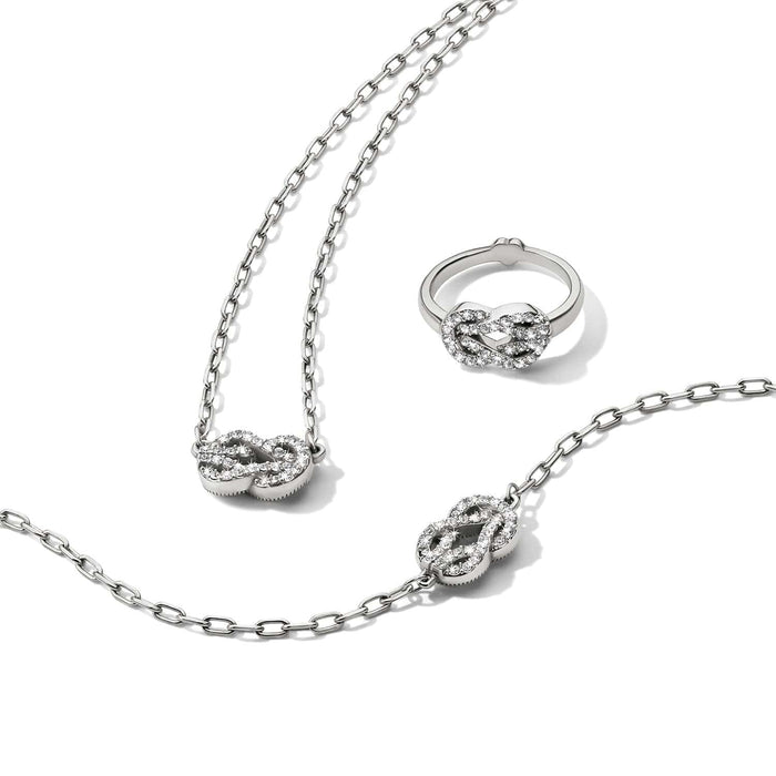 Brighton silver-plated jewelry set styled with matching knot necklace, bracelet, and ring featuring crystals on white background