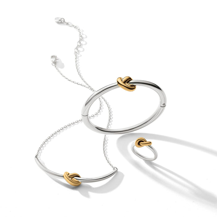Brighton two-tone jewelry set styled with silver bangle, necklace, and ring featuring gold knot accents on white