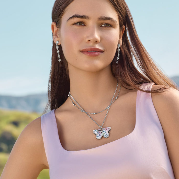 Model wearing a Brighton silver-plated butterfly pendant necklace with crystals and floral enamel, paired with crystal drop earrings