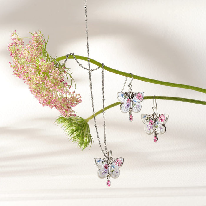Brighton butterfly necklace and earrings styled with pink flowers, featuring silver-plated floral enamel wings and crystal accents