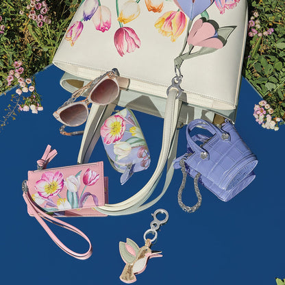 Brighton leather handbag with floral tulip print, styled with sunglasses and other accessories on a blue background