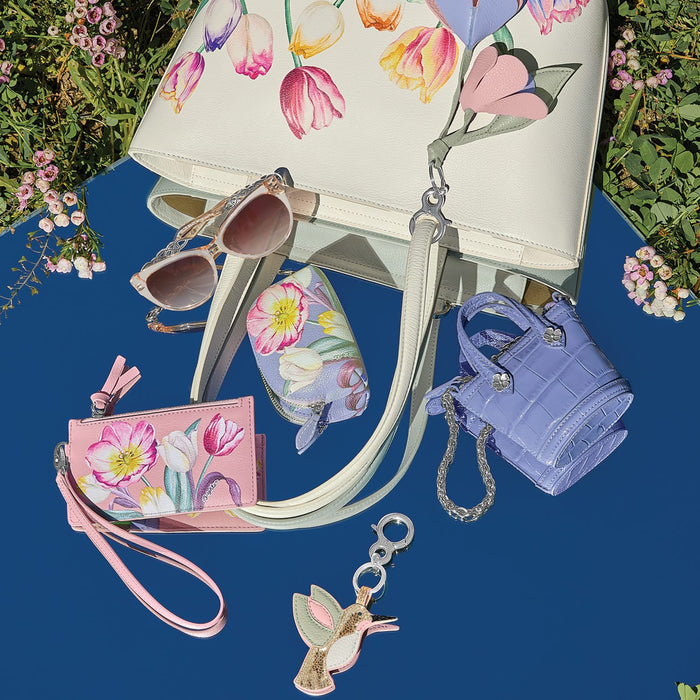 Brighton handbag with tulip floral print, styled with sunglasses and other accessories on a blue surface