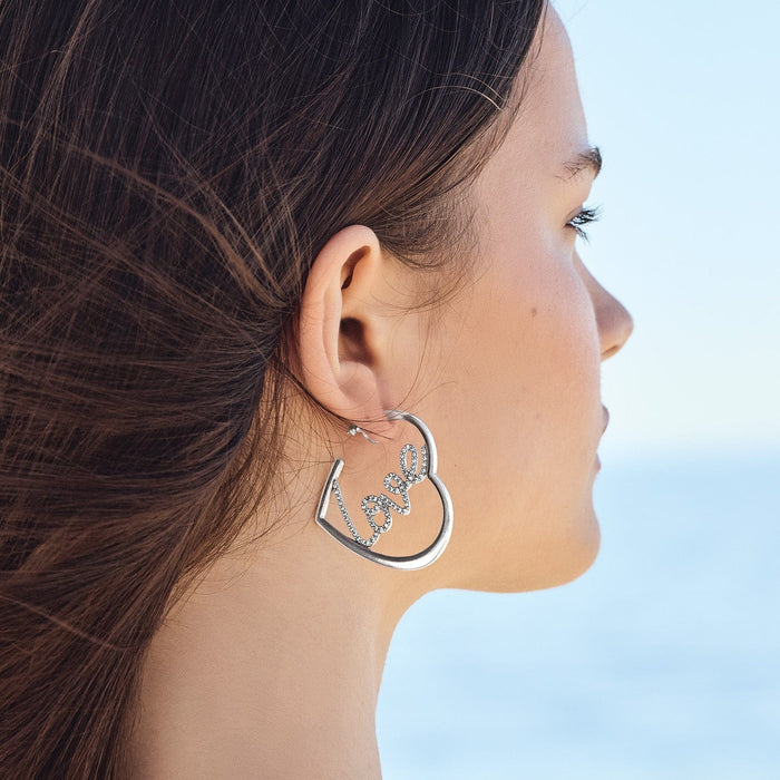 Model wearing a Brighton silver-plated heart hoop earring with crystal cursive love script detail