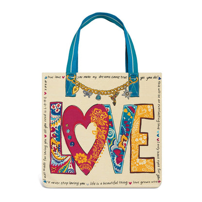 Brighton canvas tote handbag with colorful paisley LOVE print, gold charm chain, and blue handles on a white background