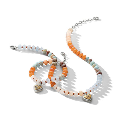Brighton beaded necklace and bracelets with orange, blue, and cream stones featuring two-tone heart charms on a white background