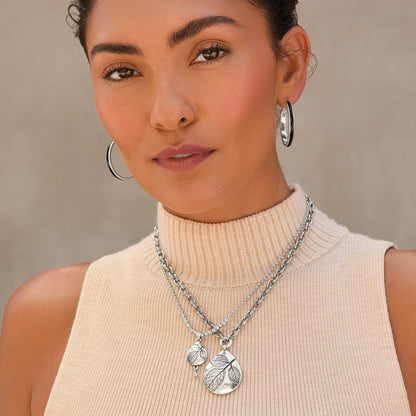Model wearing Brighton silver-plated layered necklaces with leaf-engraved teardrop pendants paired with silver-plated hoop earrings