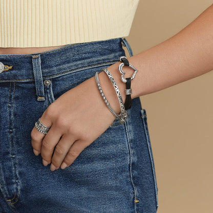 Model wearing Brighton silver-plated bangles with scroll and beaded details, paired with a black cord heart bracelet