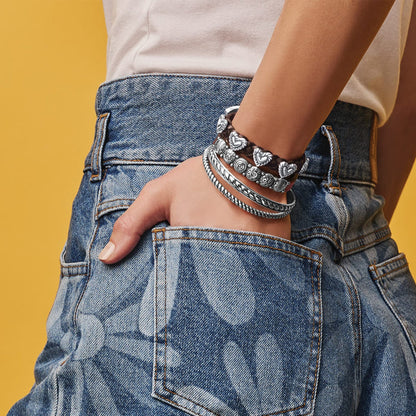 Model wearing stacked Brighton bracelets with silver-plated bangles, heart details, and braided leather band on wrist