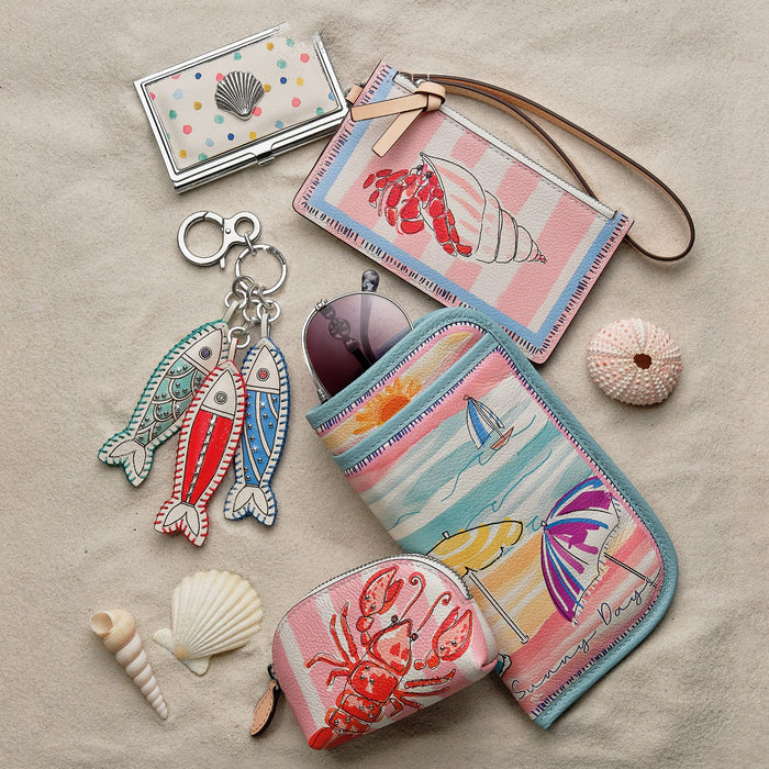 Brighton accessories styled with seashells and sunglasses on sand, featuring lobster and seashore illustrated prints.