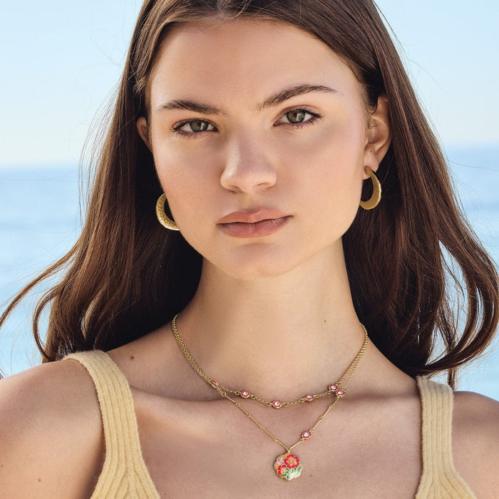 Model wearing Brighton gold-plated layered necklaces with crystal accents and enamel floral pendant, paired with hoop earrings