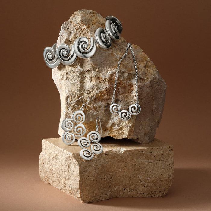 Brighton silver-plated jewelry set styled with spiral motif cuff, necklace, and earrings on stacked stone blocks